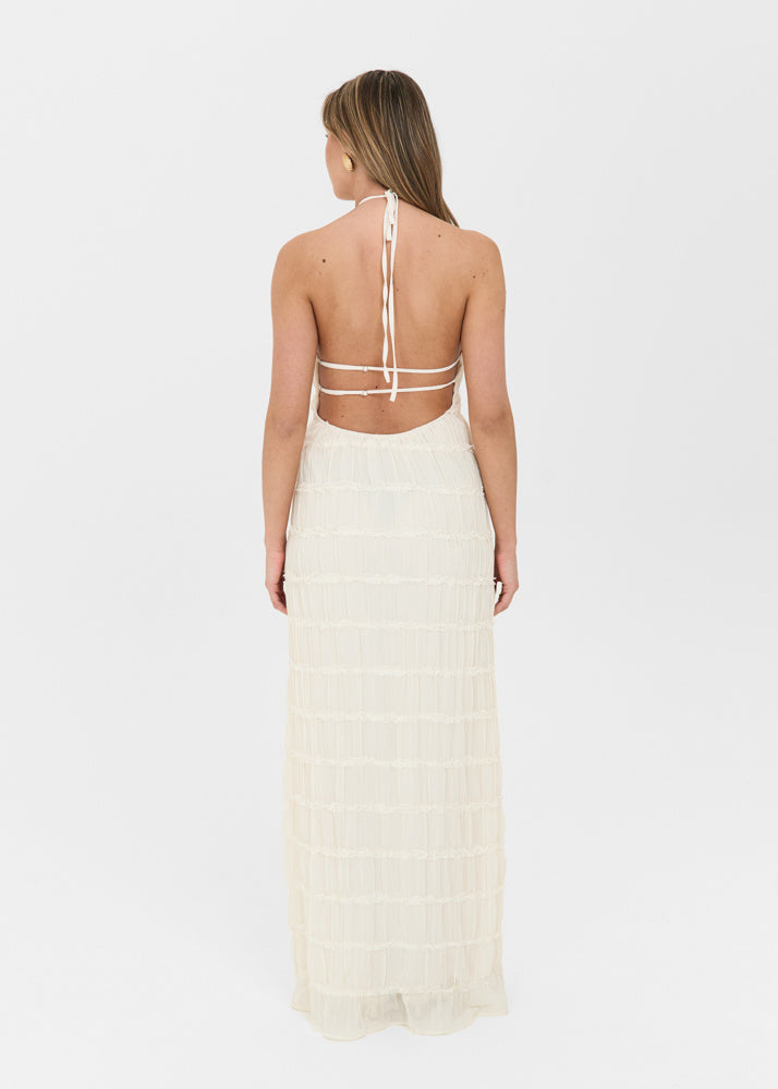 Cream-colored backless maxi dress with a halter neckline, textured tiered fabric, and ankle-length hem.