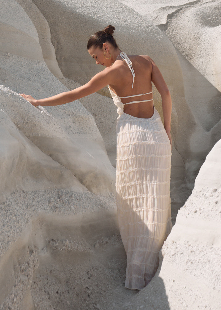 Woman wearing a cream-colored, tiered, backless halter maxi dress with a textured finish in a rocky landscape.