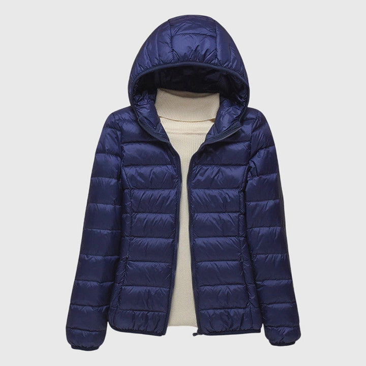 Navy blue lightweight quilted hooded jacket for women with a slim fit and full-length zip, layered over a cream sweater.