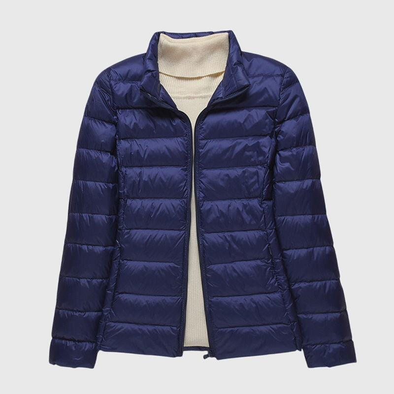 Navy blue lightweight quilted jacket with a zip-up front and stand-up collar worn over a cream ribbed sweater.