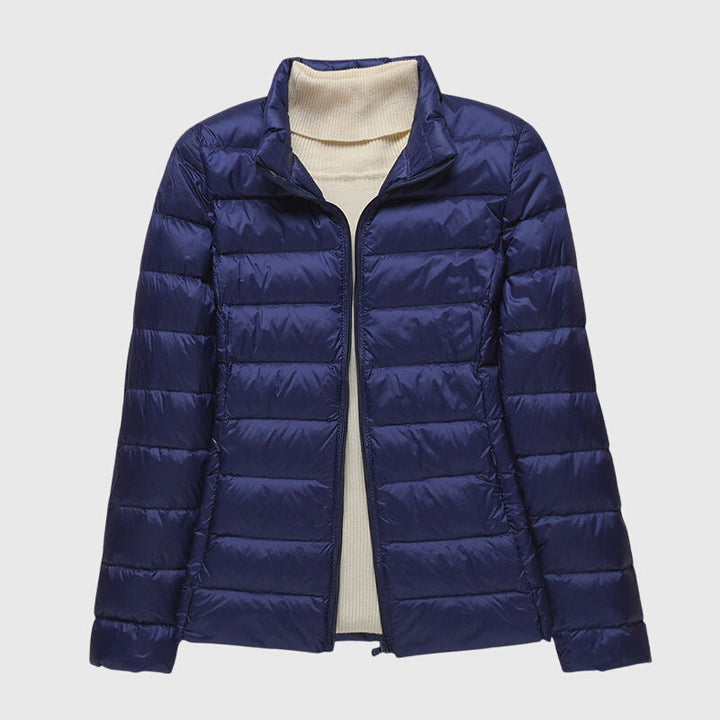 Navy blue lightweight quilted jacket with a zip-up front and stand-up collar worn over a cream ribbed sweater.