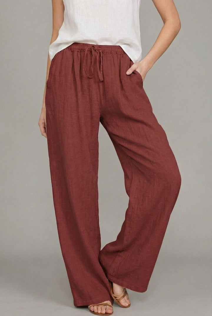 Rust-colored wide-leg linen trousers with an elasticated drawstring waist and side pockets.