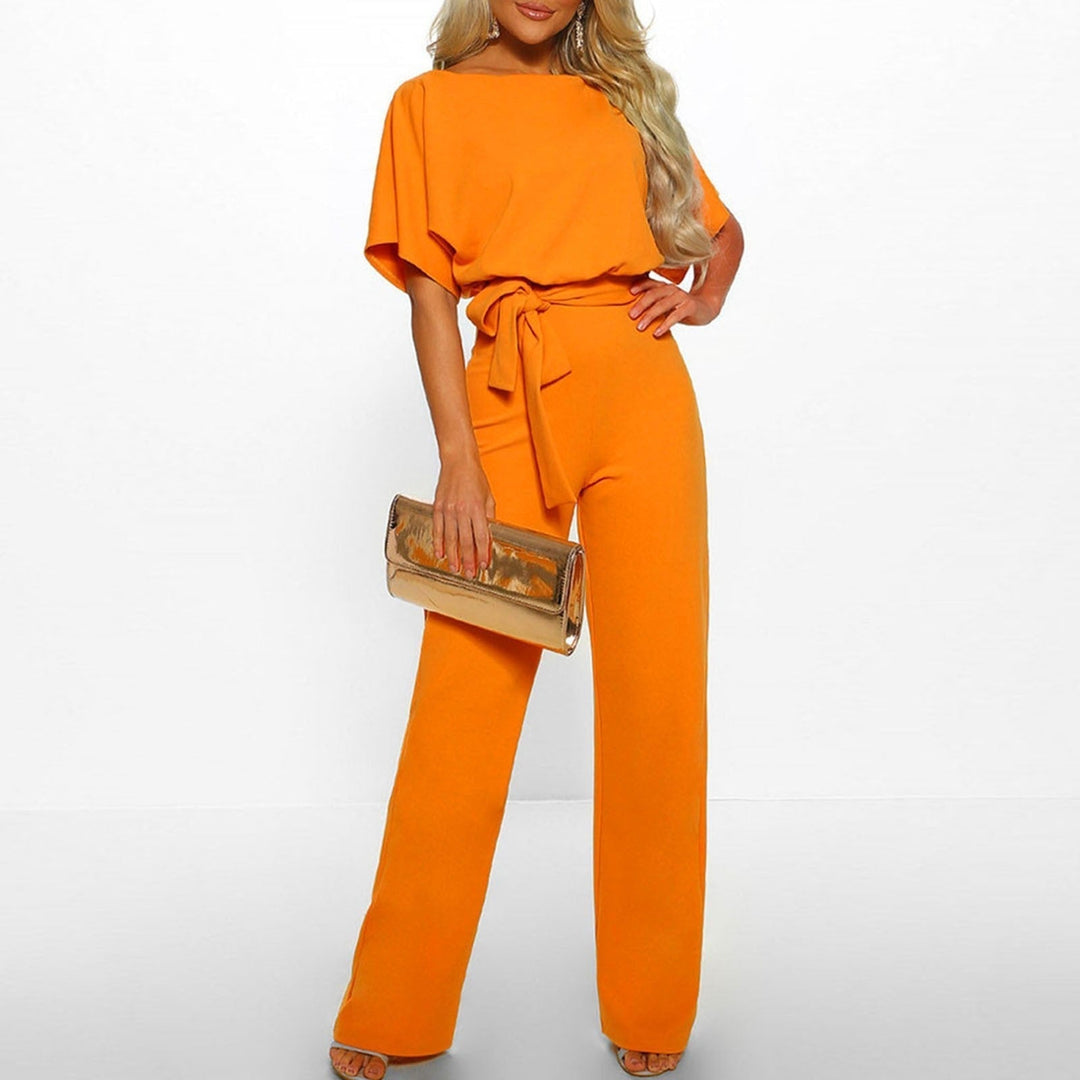 Grace women's orange tie-waist wide-leg jumpsuit with draped short sleeves and a gold clutch.