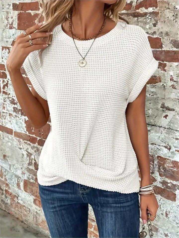White waffle knit top featuring rolled cap sleeves and a flattering twist-front hem, styled with blue jeans.
