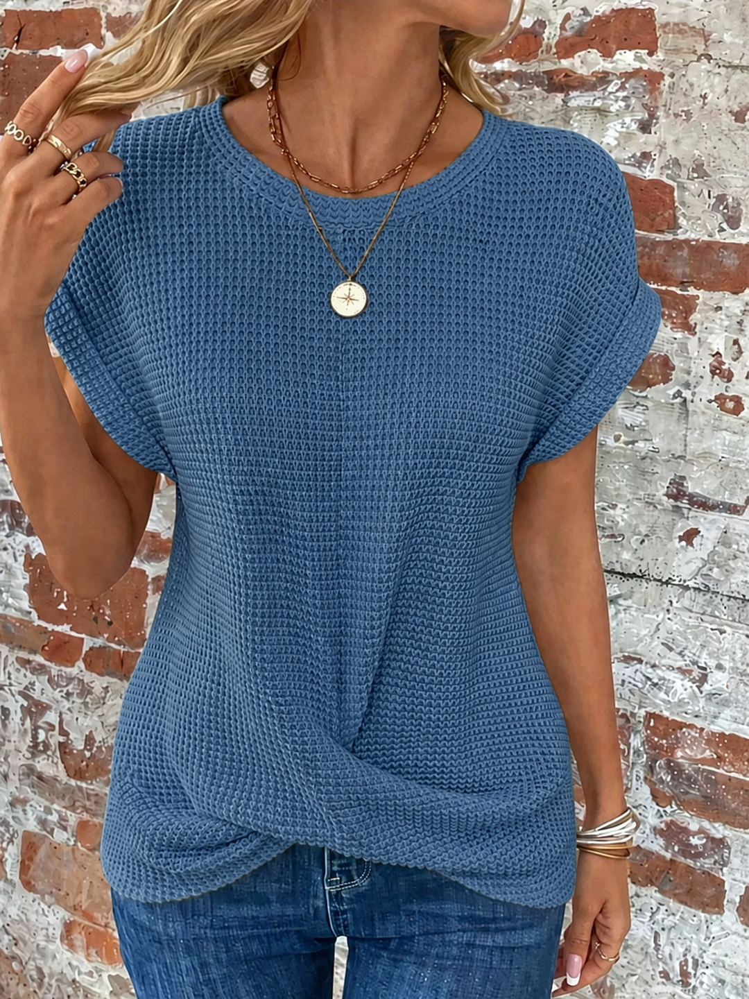 Blue waffle knit top with rolled cap sleeves and a flattering twist-front hem, styled with jeans.