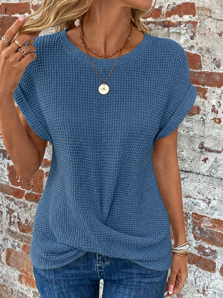 Blue waffle knit top with rolled cap sleeves and a flattering twist-front hem, styled with jeans.