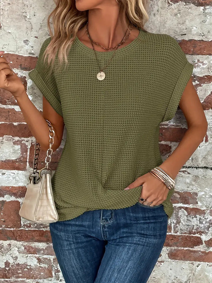 Olive green waffle knit top with rolled cap sleeves and a flattering twist-front hem, styled with blue jeans.
