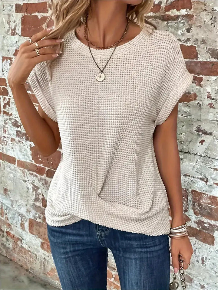 Beige waffle knit top with rolled cap sleeves and a flattering twist-front hem, styled with blue jeans.