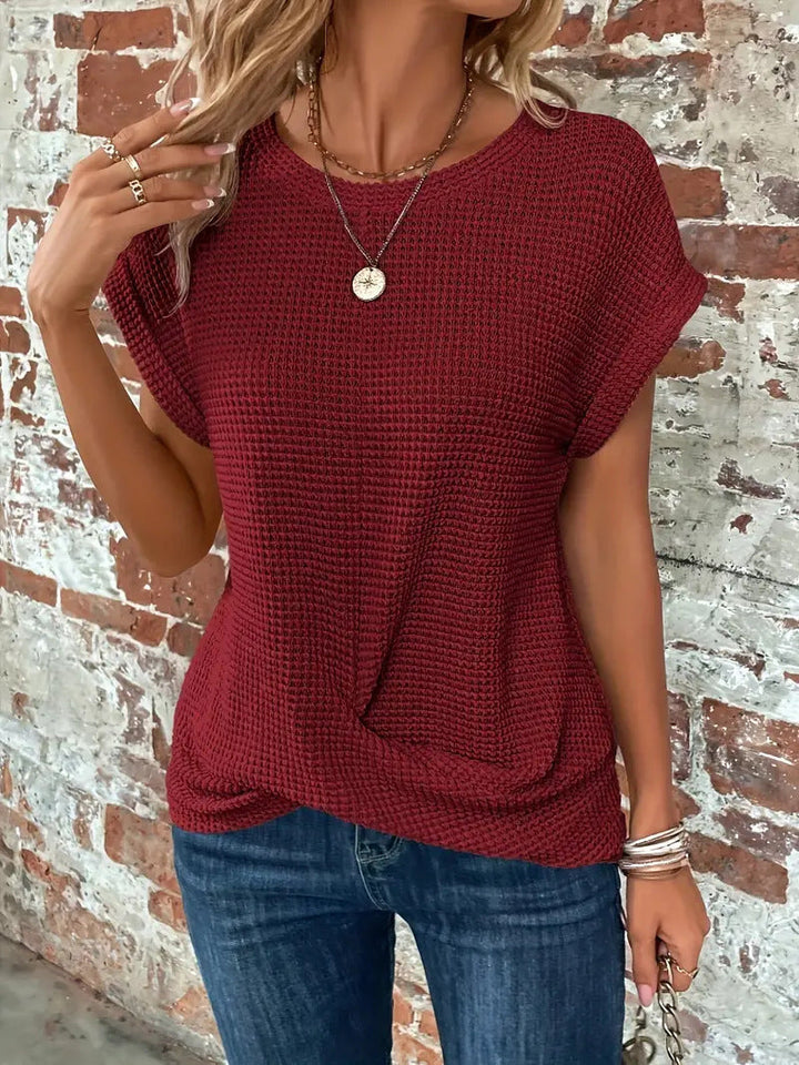 Burgundy waffle knit top featuring rolled cap sleeves and a flattering twist-front hem, styled with blue jeans.