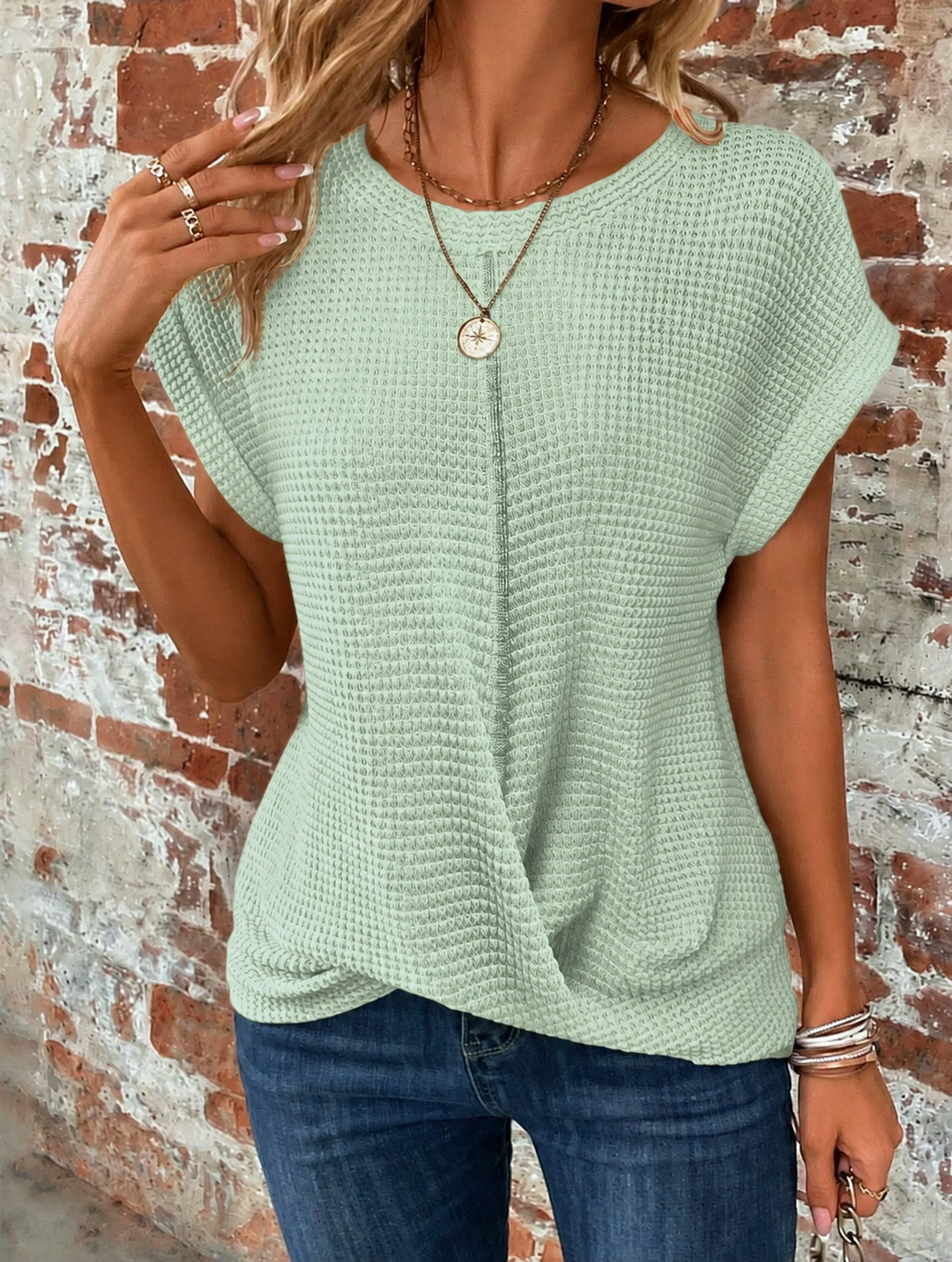 Sage green waffle knit top featuring rolled cap sleeves and a flattering twist-front hem, worn with blue jeans.