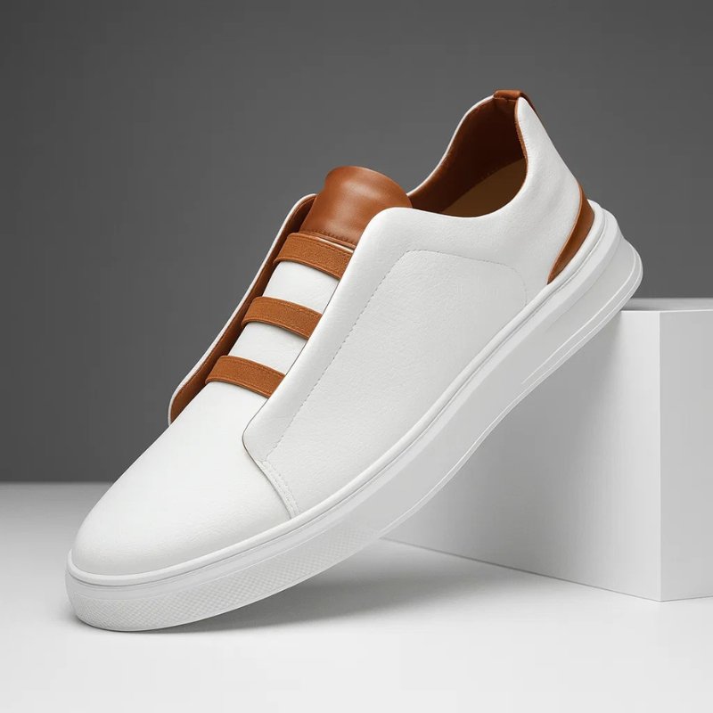 White leather slip-on trainers with tan elastic straps and a thick white rubber sole on a minimalist display.