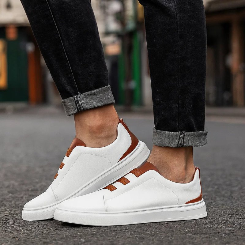 White leather slip-on trainers with brown elastic straps and trim, featuring a clean design and durable rubber sole.