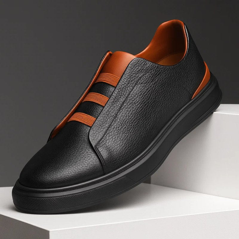Black pebbled leather slip-on trainer with orange elastic straps and a thick black rubber sole.