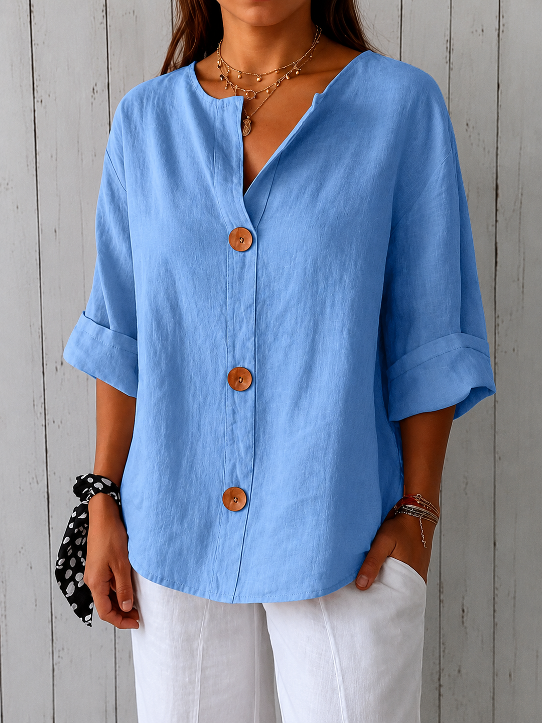 Relaxed blue linen V-neck blouse with three-quarter rolled sleeves and statement wooden buttons.