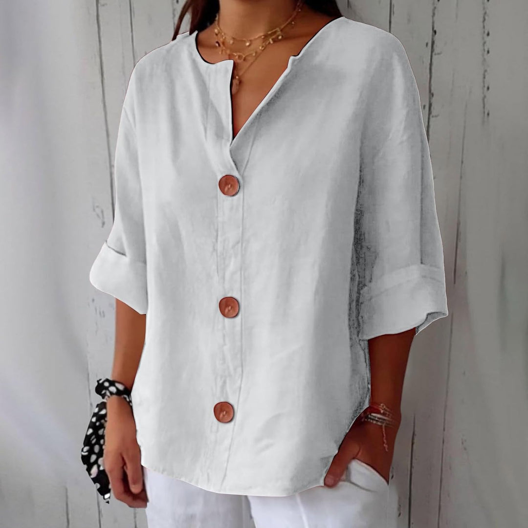 White linen V-neck blouse with three-quarter rolled sleeves and large wooden buttons in a relaxed, loose fit.