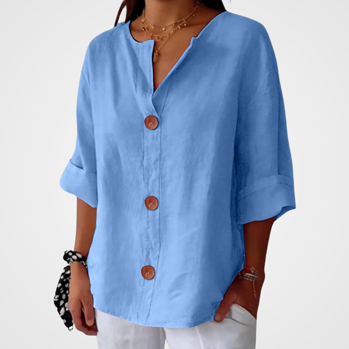 Blue linen V-neck blouse with three-quarter rolled sleeves and large wooden buttons in a relaxed, loose-fitting style.