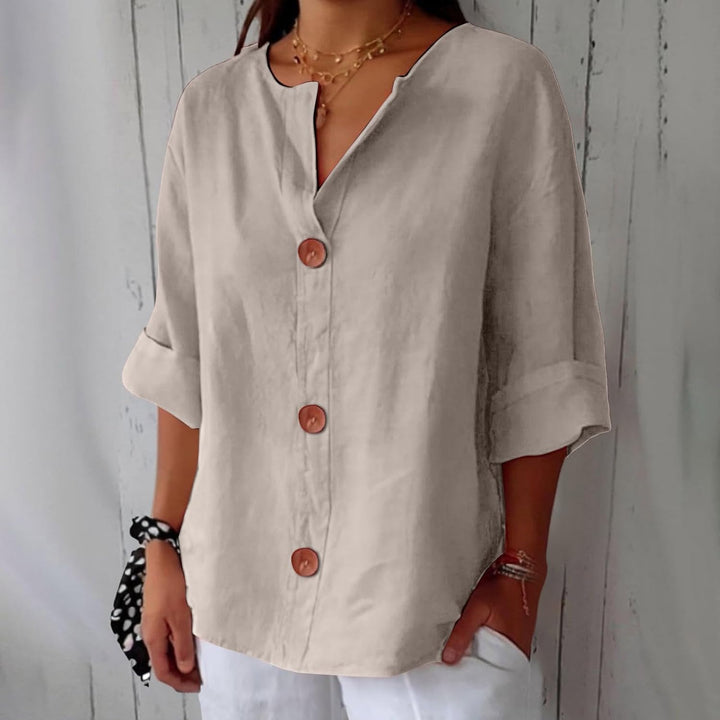 Beige linen V-neck blouse with three-quarter rolled sleeves and large wooden buttons in a relaxed, loose fit.