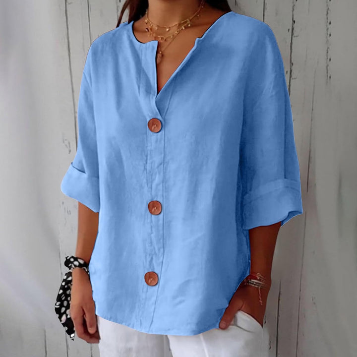 Blue linen V-neck blouse with three-quarter rolled sleeves and statement wooden buttons in a relaxed, loose fit.