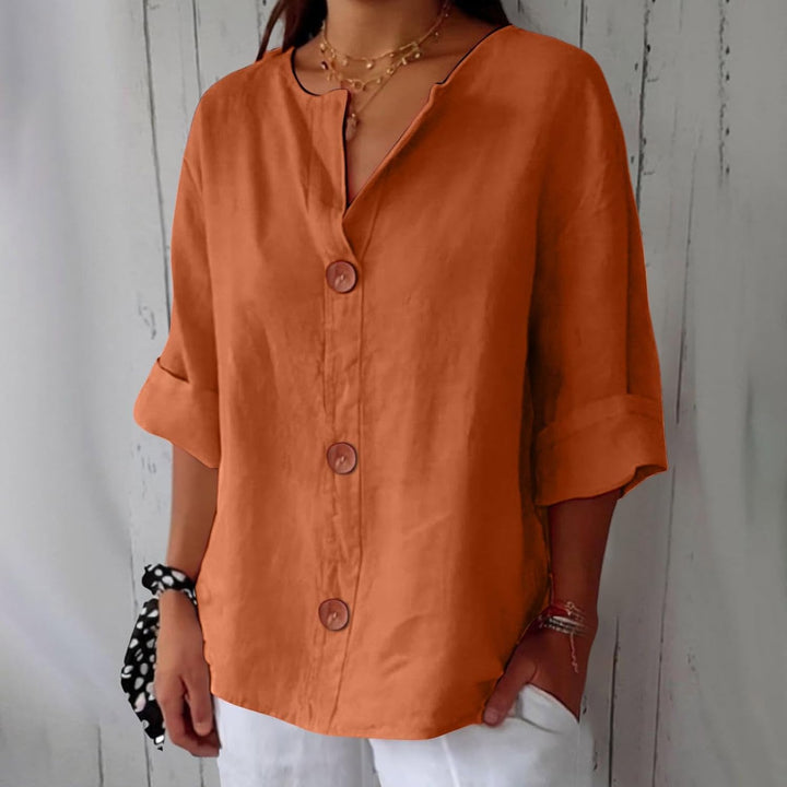 Rust orange linen V-neck blouse with wooden buttons and rolled three-quarter sleeves.