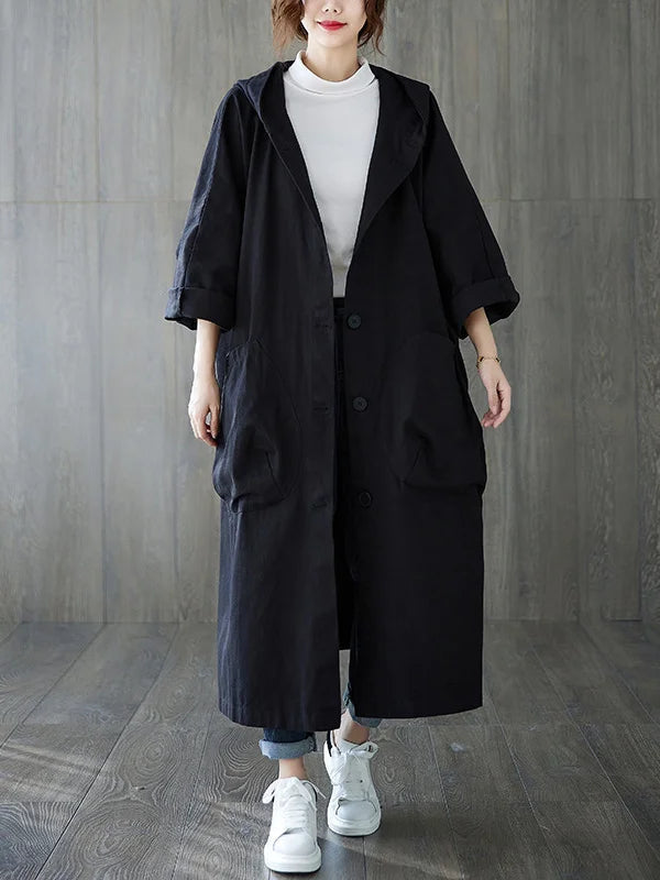 Black longline hooded coat with an oversized fit, button front, and large patch pockets worn over jeans and sneakers.