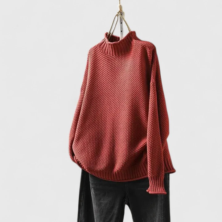 Rust-red mock neck knitted jumper with a textured finish, dropped shoulders, and ribbed trim, hanging on a hanger.