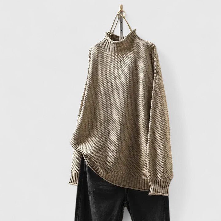 Beige textured mock neck knitted jumper with dropped shoulders and ribbed hem, hanging above black trousers.