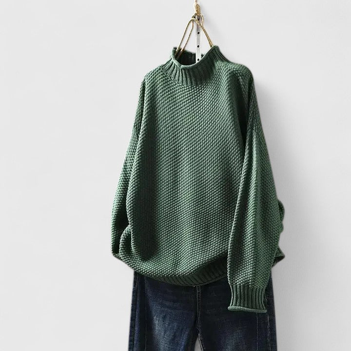Green textured mock neck jumper with dropped shoulders and ribbed trim, hanging above dark blue denim jeans.