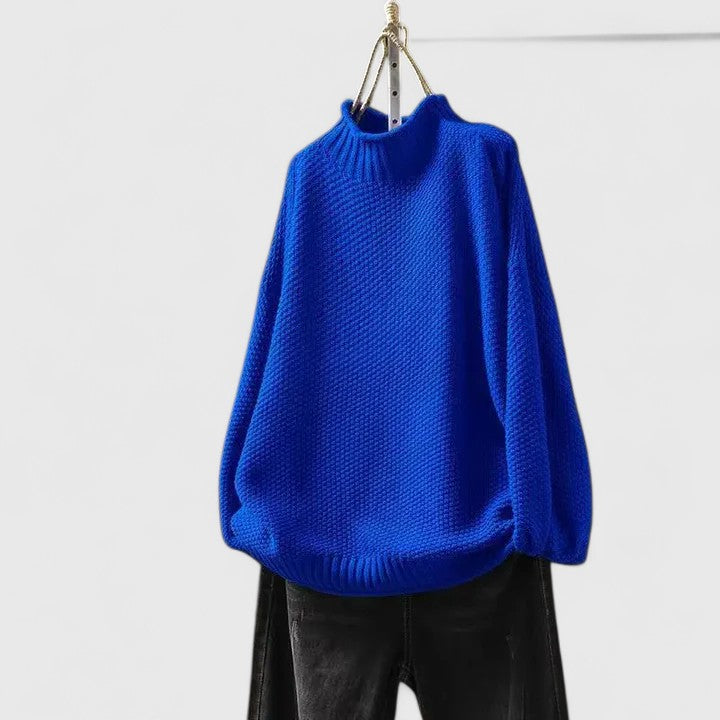 Bright blue mock neck knitted jumper with textured fabric, dropped shoulders, and ribbed trim, paired with black jeans.