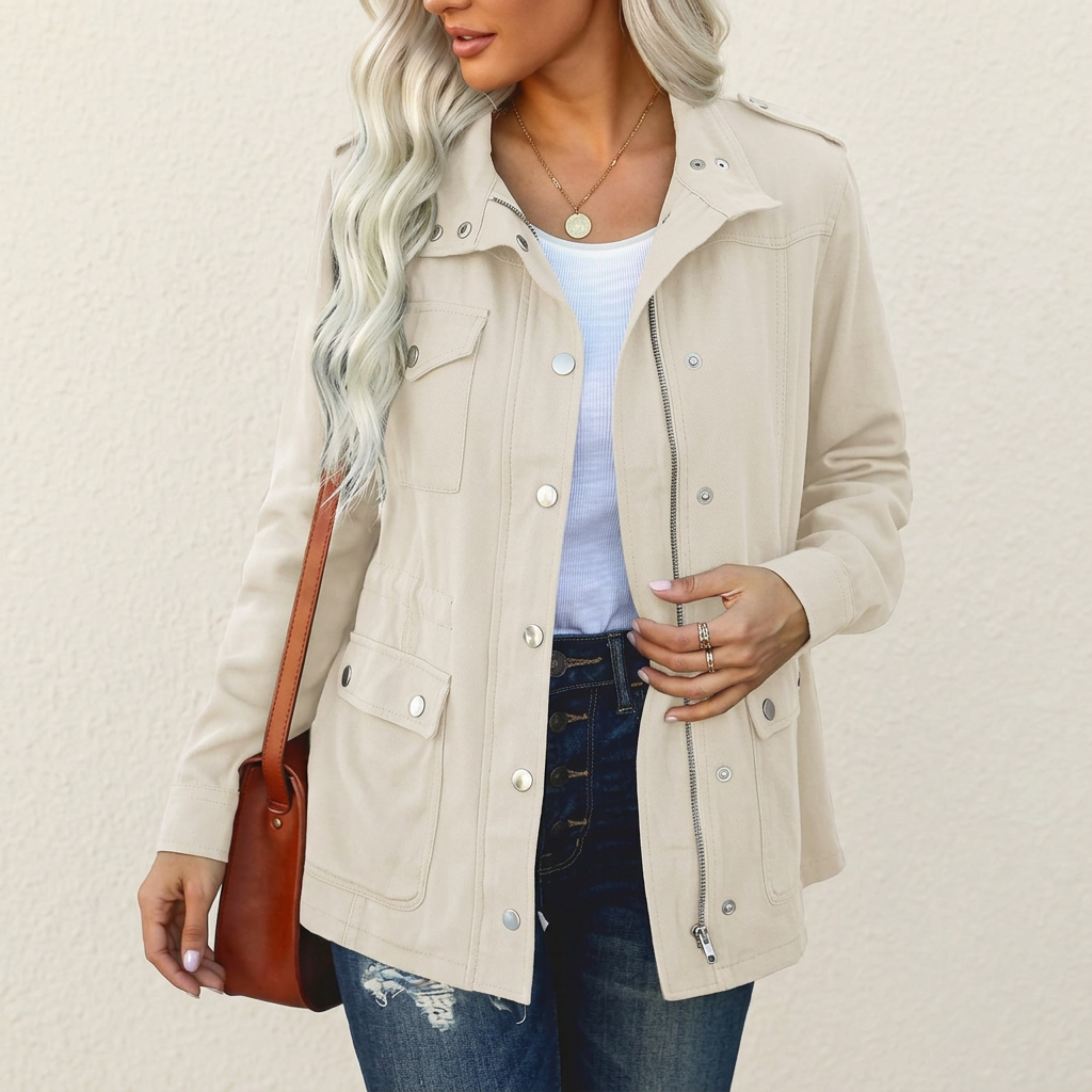 Beige utility jacket with shoulder tabs, flap pockets, zip and snap-button front, worn over a white top and blue jeans.