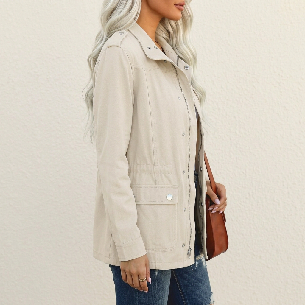 Beige utility jacket with shoulder tabs, flap pockets, and a full-length zip closure worn over blue denim jeans.