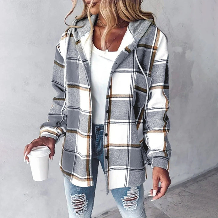 Woman wearing a grey, white, and tan checked hooded jacket with a button-front closure over a white top and distressed jeans.