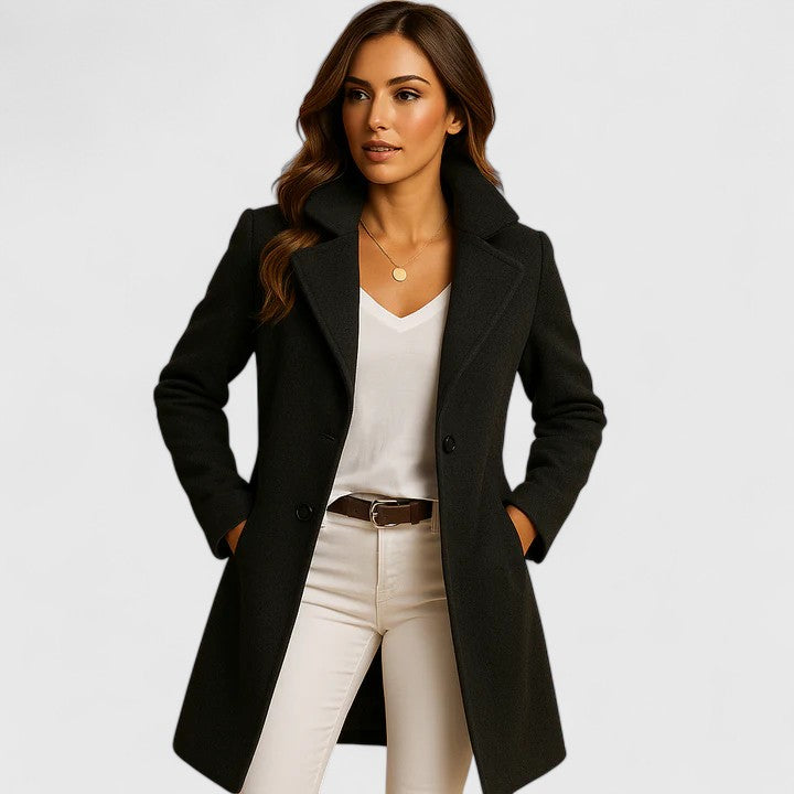 Woman wearing a charcoal grey longline tailored coat with notched lapels and button front closure over white trousers.