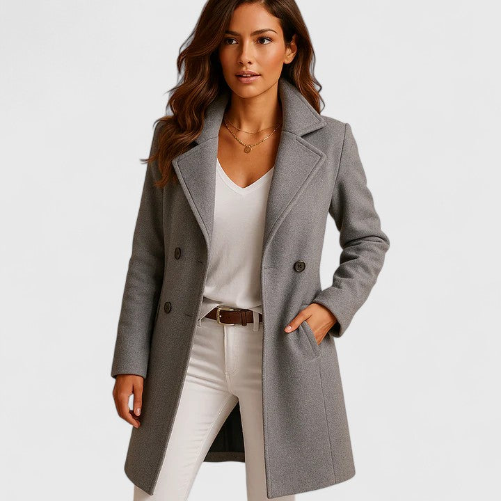 Woman wearing a grey longline tailored coat with notched lapels and a button-front closure over a white top and jeans.