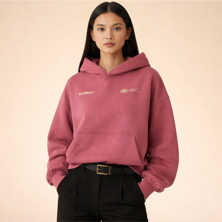 Woman wearing a dusty rose oversized pullover hoodie with a front kangaroo pocket and subtle logo embroidery.