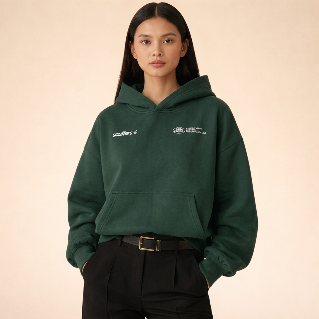 Model wearing a forest green oversized pullover hoodie with a lined hood, kangaroo pocket, and white logo detailing.