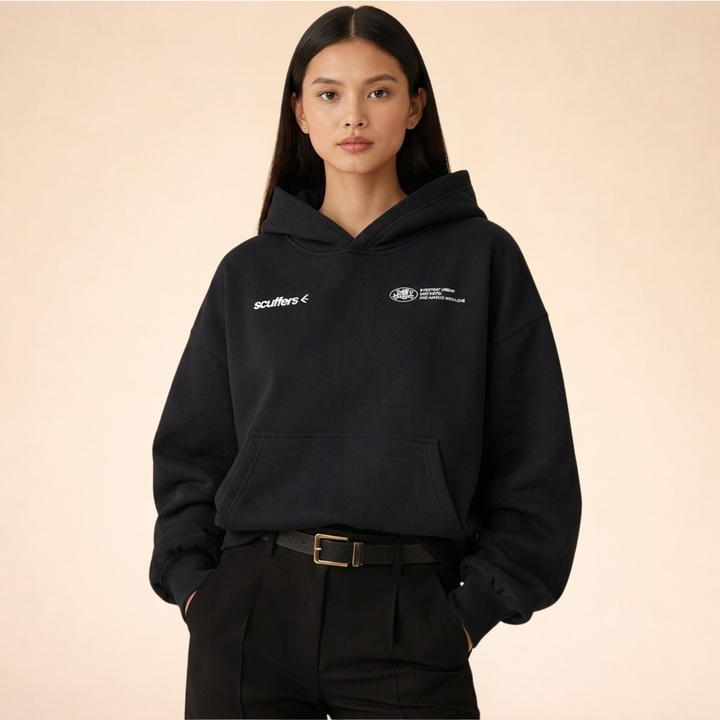 Model wearing a black oversized pullover hoodie with a lined hood, ribbed cuffs, kangaroo pocket, and white logo detailing.