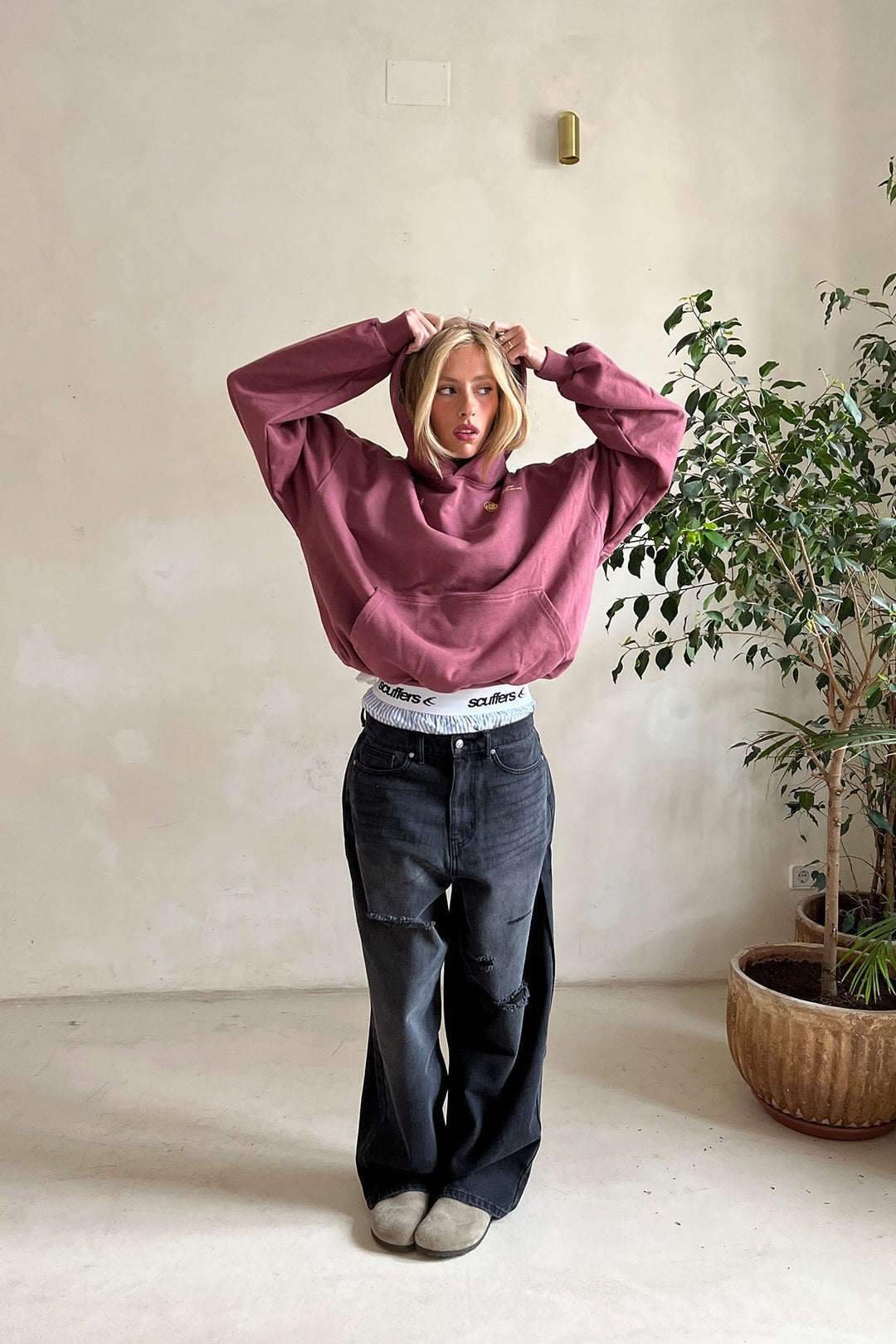 Woman wearing a plum-colored oversized pullover hoodie with a kangaroo pocket, ribbed cuffs, and a lined hood.