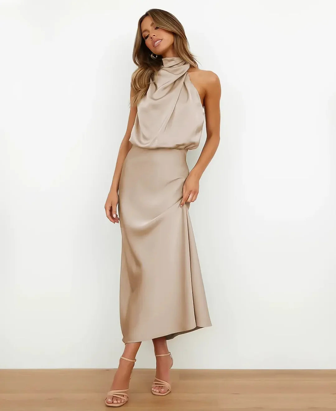 Woman wearing a champagne satin halter maxi dress with a draped blouson bodice and floor-length skirt.