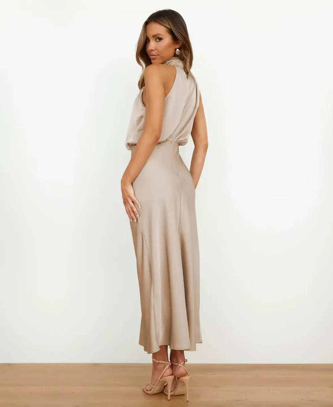 Woman wearing a champagne satin halter maxi dress with a blouson bodice and floor-skimming silhouette.