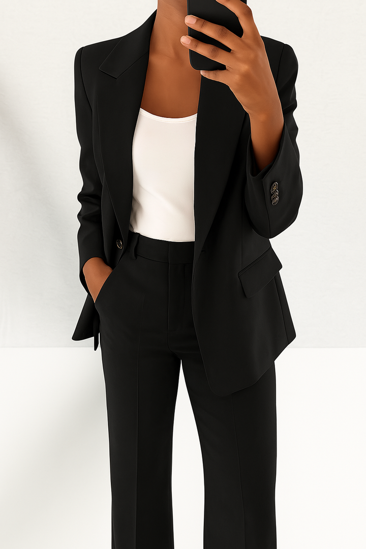 Woman wearing a black tailored single-button blazer and matching straight-leg trousers with a white top.
