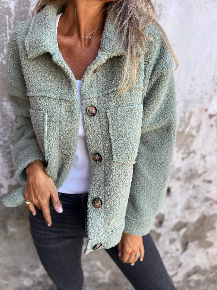 Sage green teddy jacket with a button-front, spread collar, and chest pockets worn over a white top and black jeans.