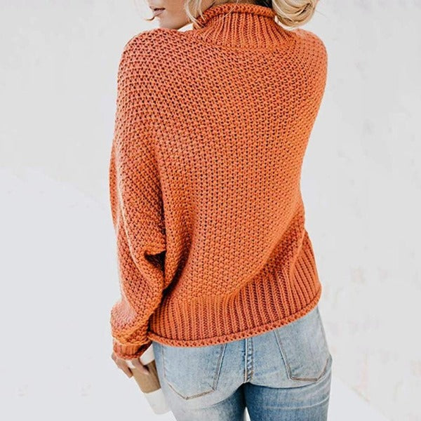Woman wearing a burnt orange chunky knit turtleneck jumper with dropped sleeves, ribbed hem, and a relaxed fit.