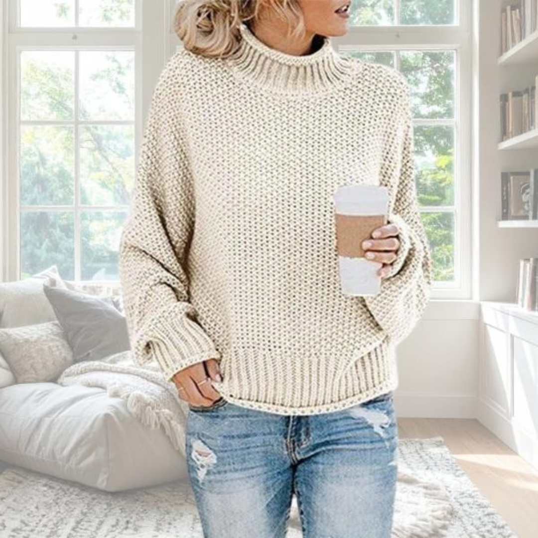 Cream chunky knit turtleneck jumper with a relaxed fit, dropped sleeves, and ribbed trim, worn with blue jeans.