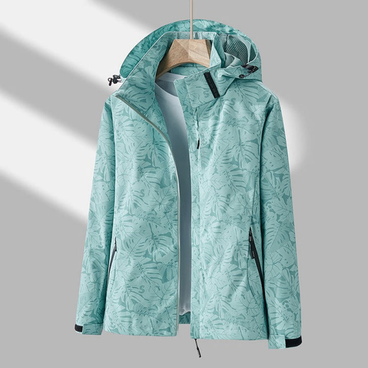 Light green waterproof jacket with a tropical leaf print, featuring an adjustable hood, full-length zip, and side pockets.