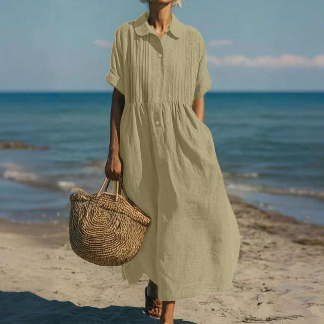 Olive green linen-look maxi shirt dress with pintuck bodice, button placket, and short sleeves worn on the beach.