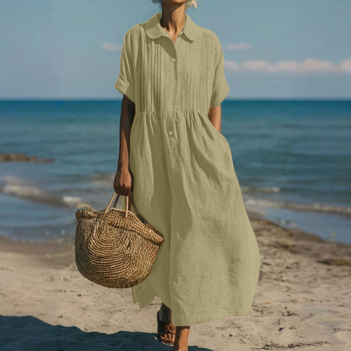 Olive green linen-look maxi shirt dress with pintuck bodice, button placket, and short sleeves worn on the beach.