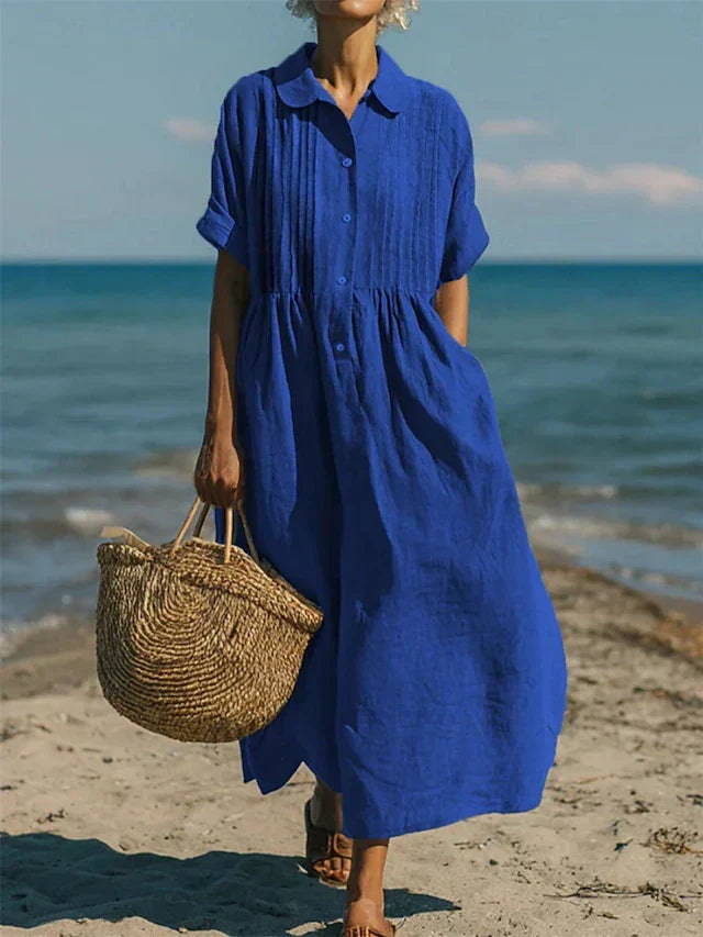 Royal blue linen-look maxi shirt dress with pintuck bodice, button placket, and short sleeves on a beach.