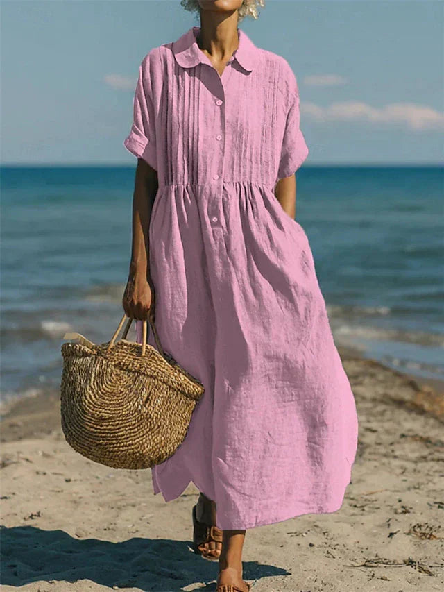 Pink linen-look maxi shirt dress with pintuck bodice, button placket, and short sleeves, worn on a beach.