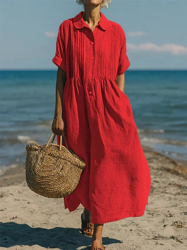 Red linen-look maxi shirt dress with pintuck bodice, button placket, and short sleeves, worn on a beach.