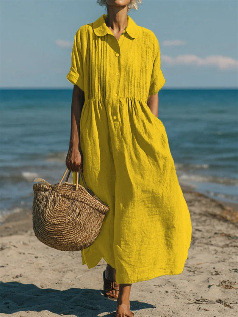 Bright yellow linen-look maxi shirt dress with pintuck bodice, button placket, and short sleeves on a beach.